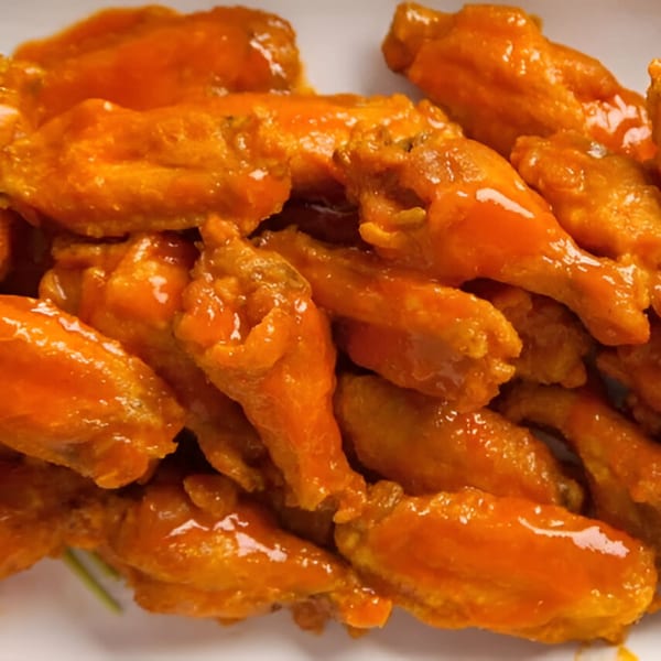 A close-up of a pile of Devil's Pizzeria's hot wings, glistening with orange sauce.