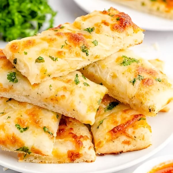 A stack of golden-brown Devil's Pizzeria garlic breadsticks, topped with melted cheese and green herbs.